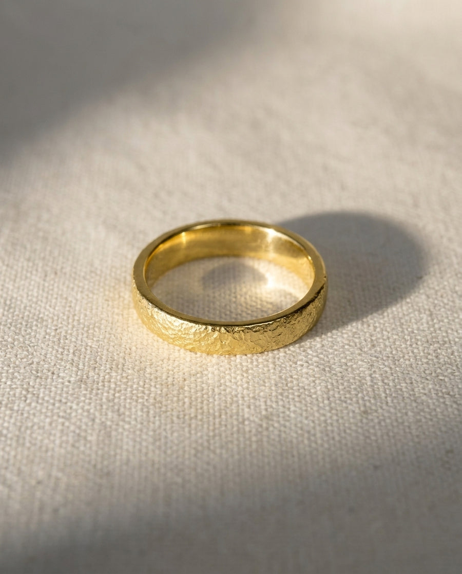 Gold wedding band with a textured, hammered finish resting on a light fabric surface.
