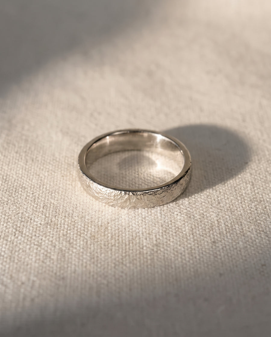 Silver wedding band with a textured, hammered finish resting on a light fabric surface.