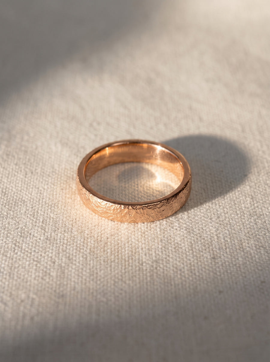 Rose gold wedding band with a textured, hammered finish resting on a light fabric surface.