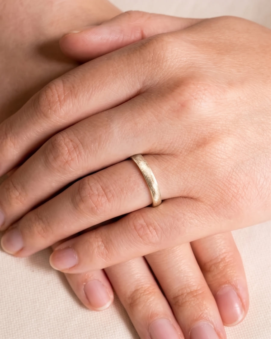 Gold textured court wedding band worn on a finger, featuring a matte finish and rounded profile.