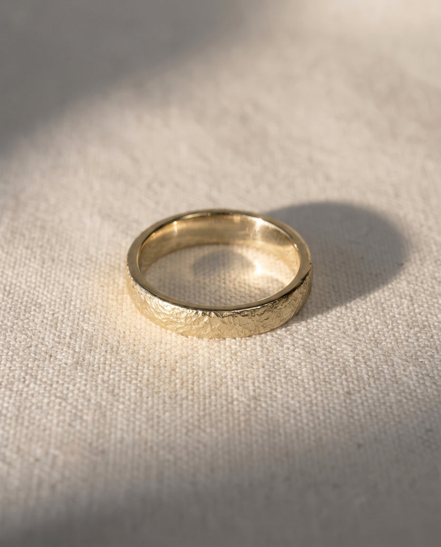 Gold wedding band with a textured, hammered finish resting on a light fabric surface.