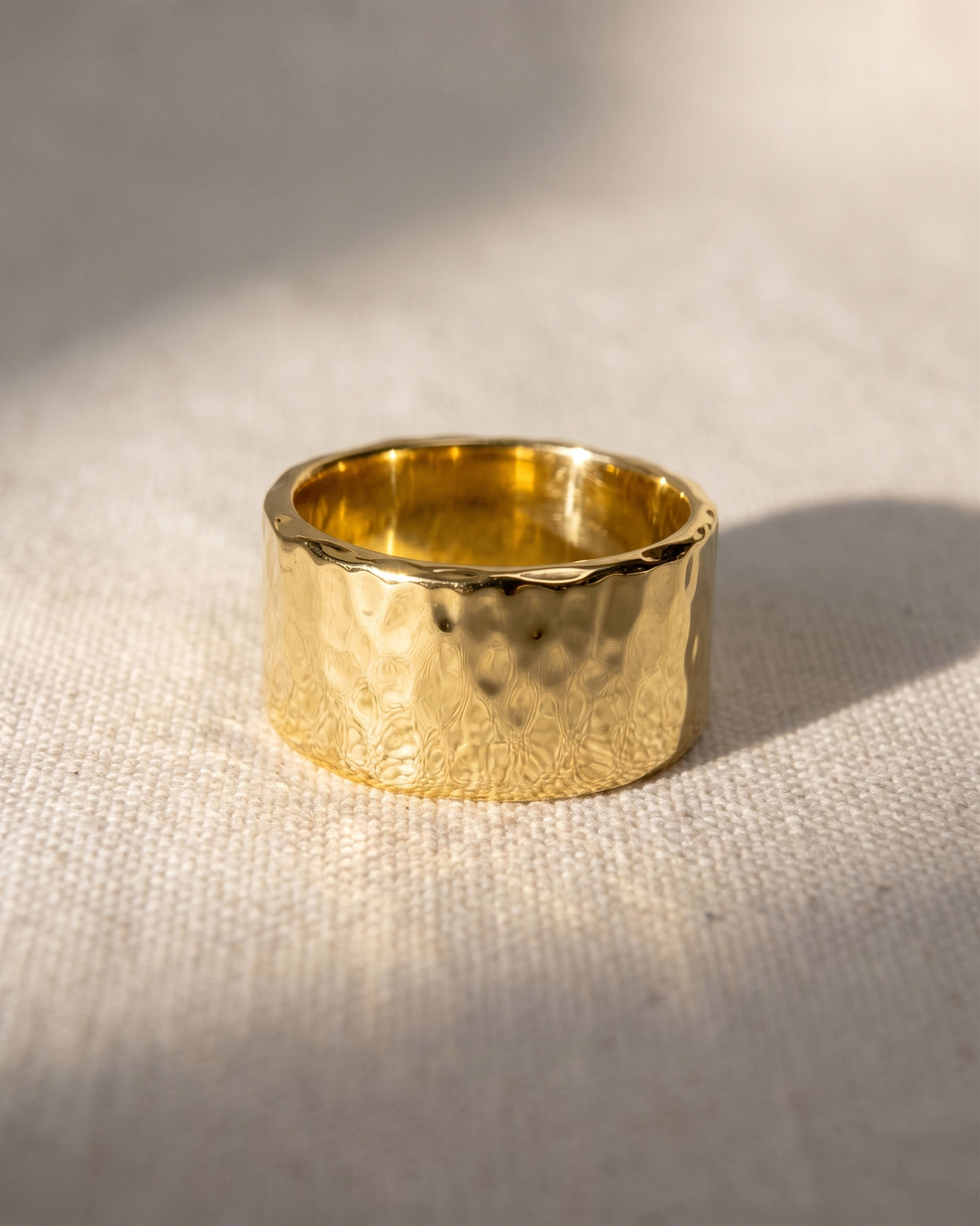 Wide gold wedding band with a textured, hammered finish resting on a light fabric surface.
