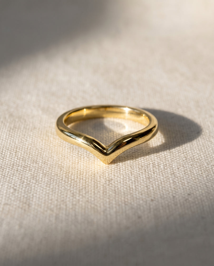 Polished gold wishbone wedding ring with a V-shaped design resting on a textured cream fabric surface.