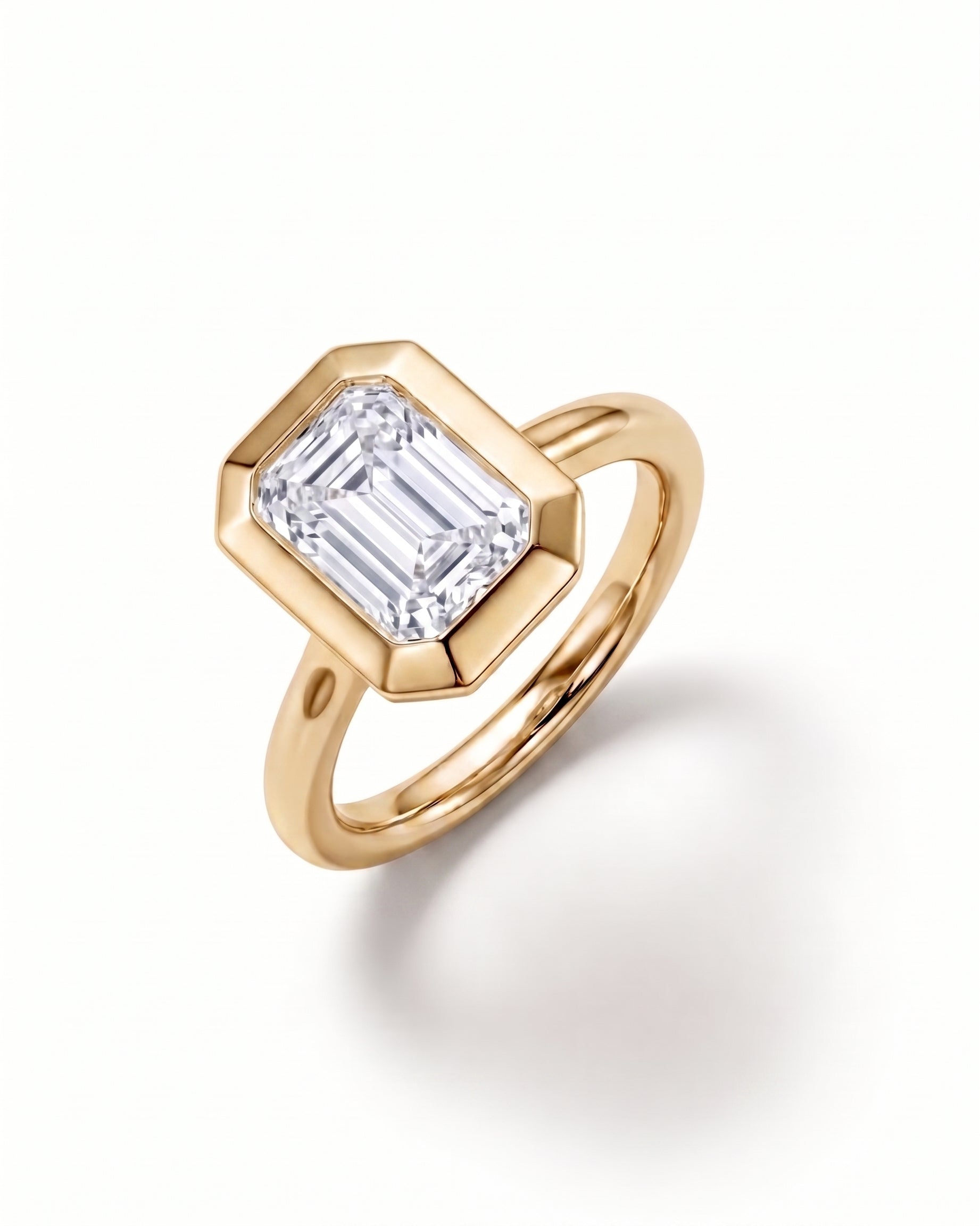 Emerald cut diamond engagement ring in a gold bezel setting with a cathedral band.