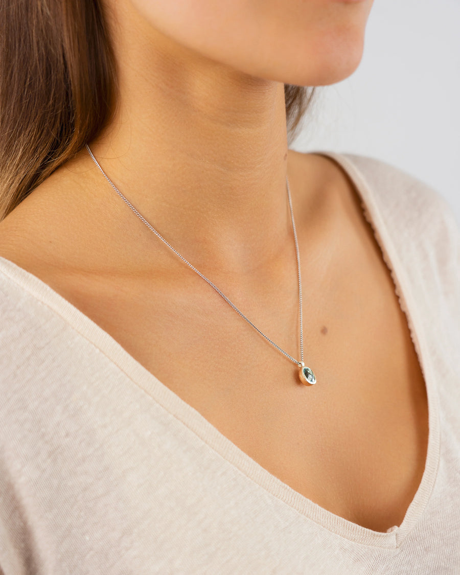 Woman wearing a delicate silver necklace with an oval gemstone pendant