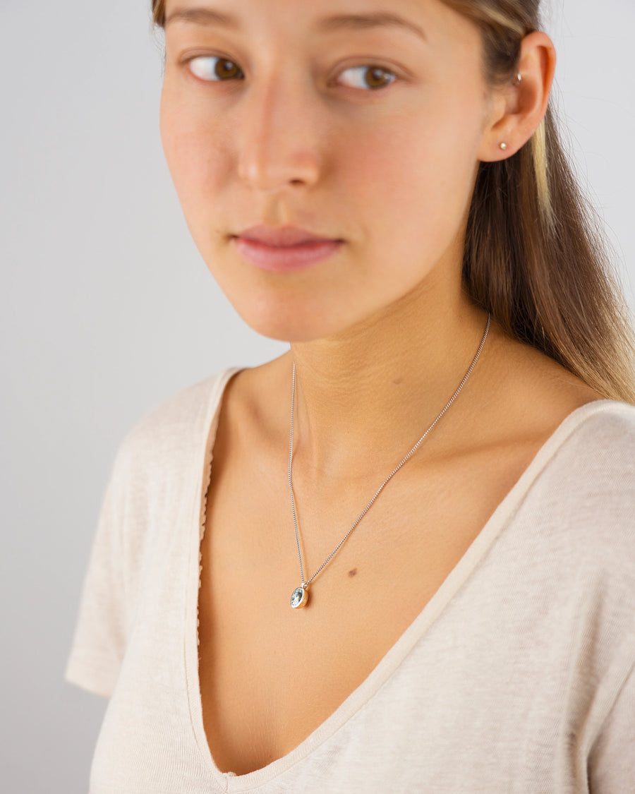 Woman wearing a minimalist pendant necklace with a light blue gemstone on a fine chain