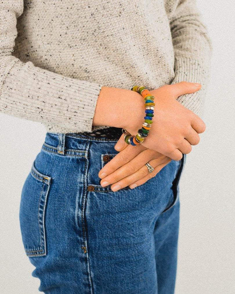 Handmade recycled glass bead bracelet with vibrant colors on a person wearing jeans