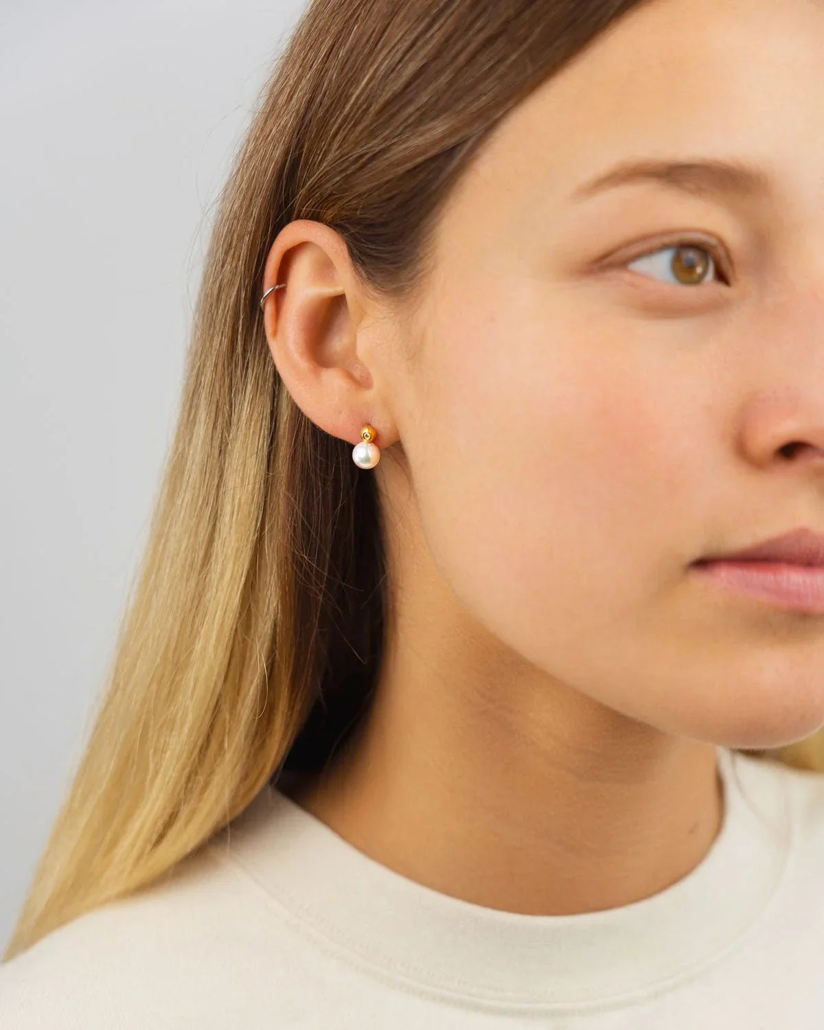 Woman wearing gold stud earrings with diamond and Akoya pearl on light background
