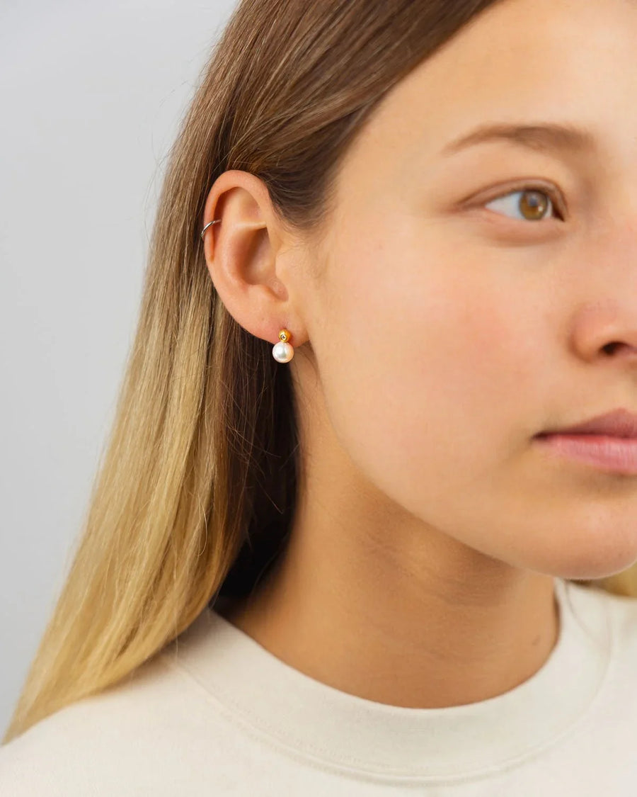 Woman wearing gold stud earrings with diamond and Akoya pearl on light background