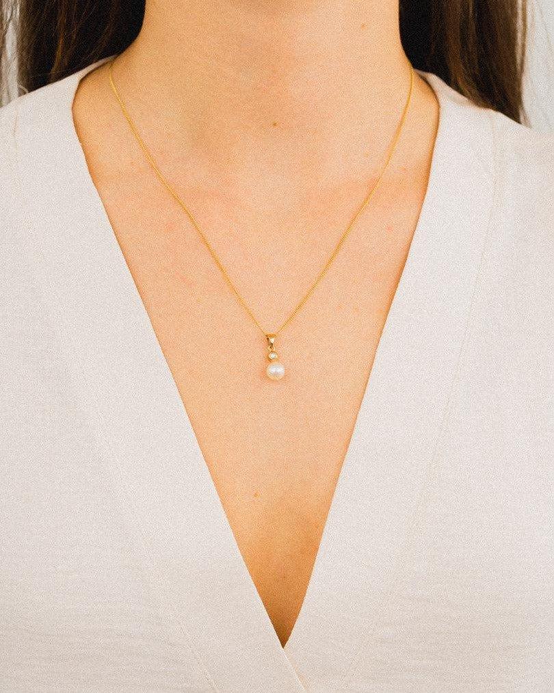 Gold chain necklace with diamond and Akoya pearl pendant on woman in white blouse