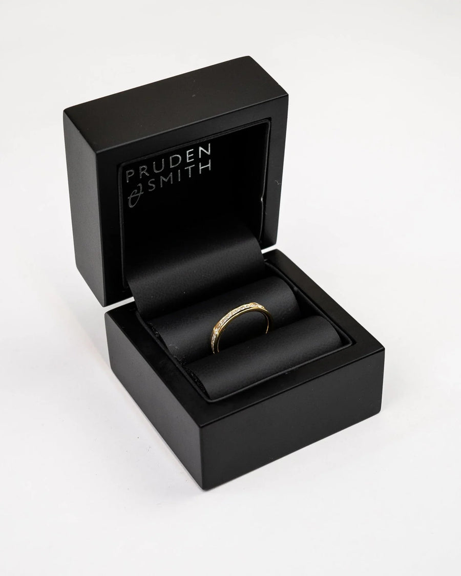 Gold eternity ring with alternating rubies and diamonds in a black box.