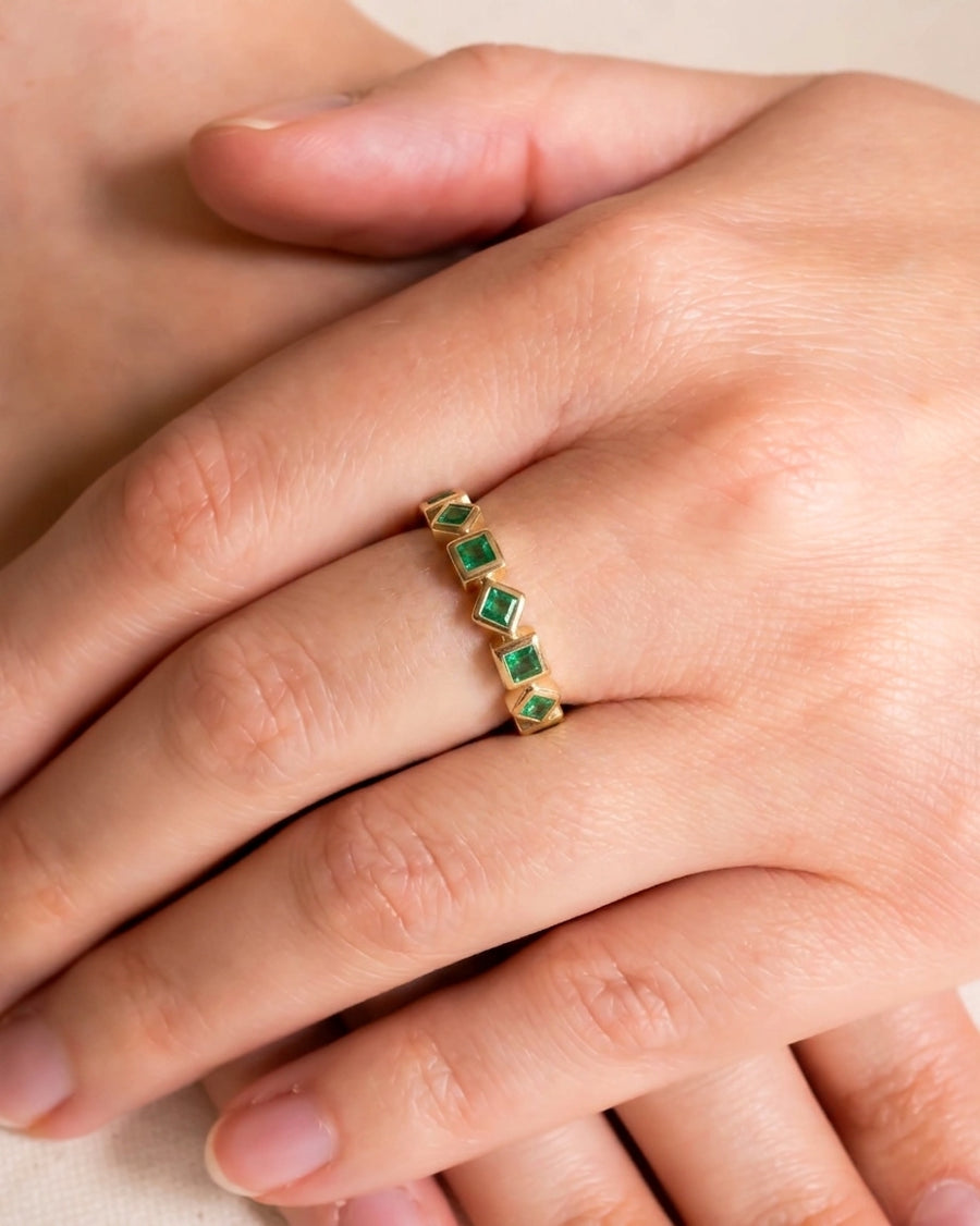 Gold eternity ring with alternating square emeralds on a hand.