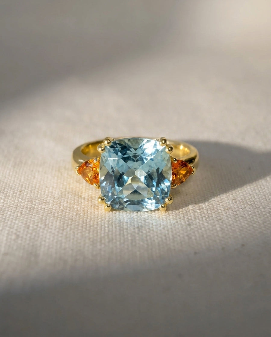 18ct yellow gold ring with a cushion-cut aquamarine and two triangular orange sapphires.