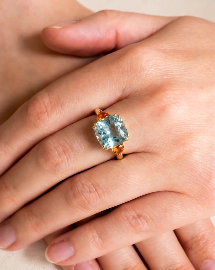 Gold dress ring with a cushion-cut aquamarine and two orange sapphires.