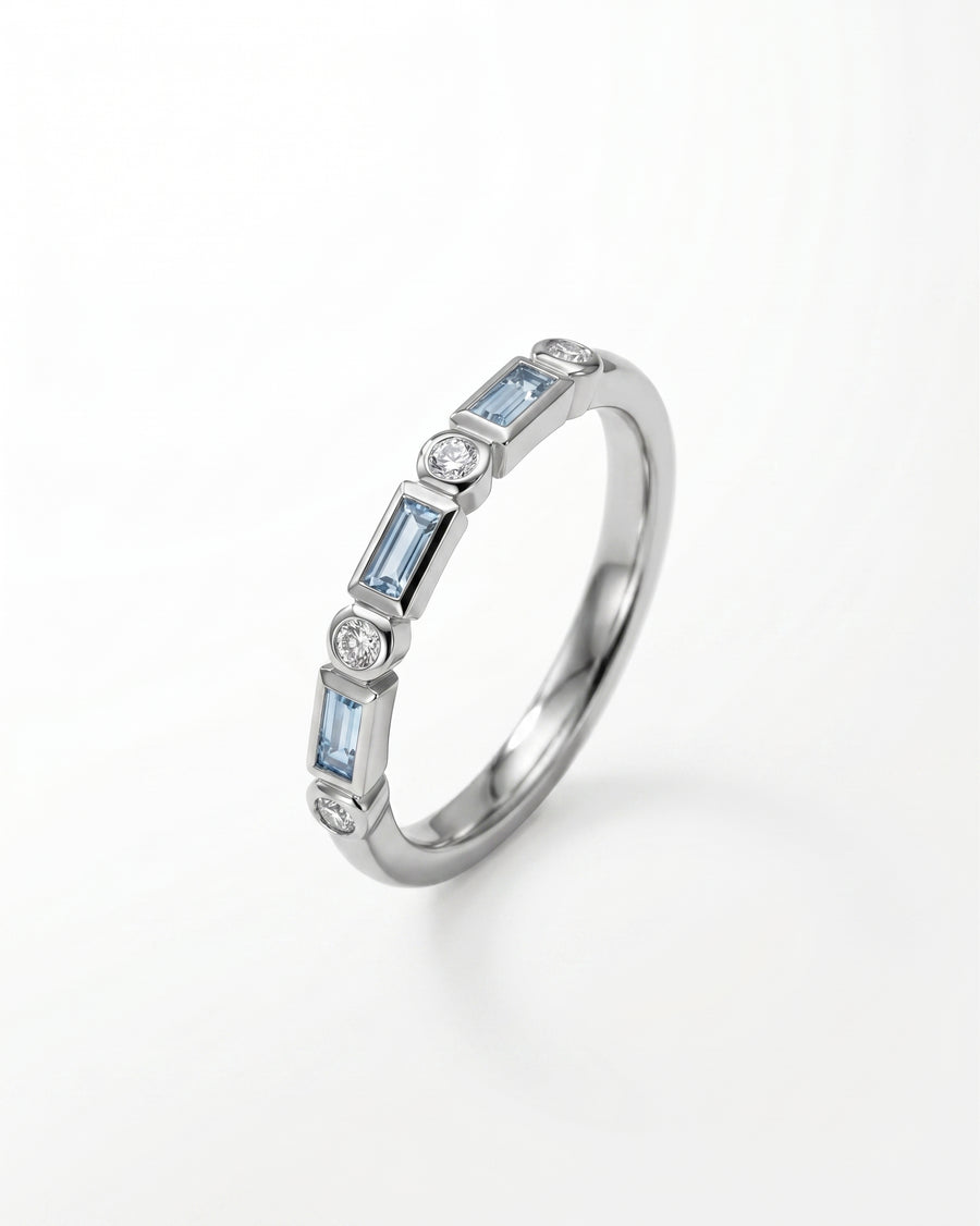 Platinum eternity ring featuring alternating baguette-cut aquamarines and round brilliant diamonds in a bezel setting.
