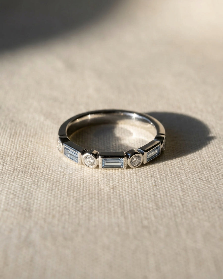 Platinum half eternity ring featuring alternating baguette aquamarines and round diamonds in bezel settings.