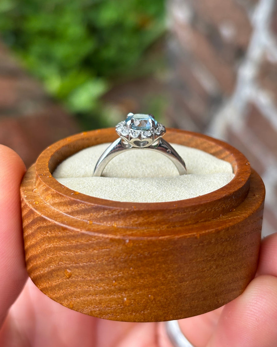 Aquamarine ring in a white gold scalloped diamond cluster setting held in a wooden box.