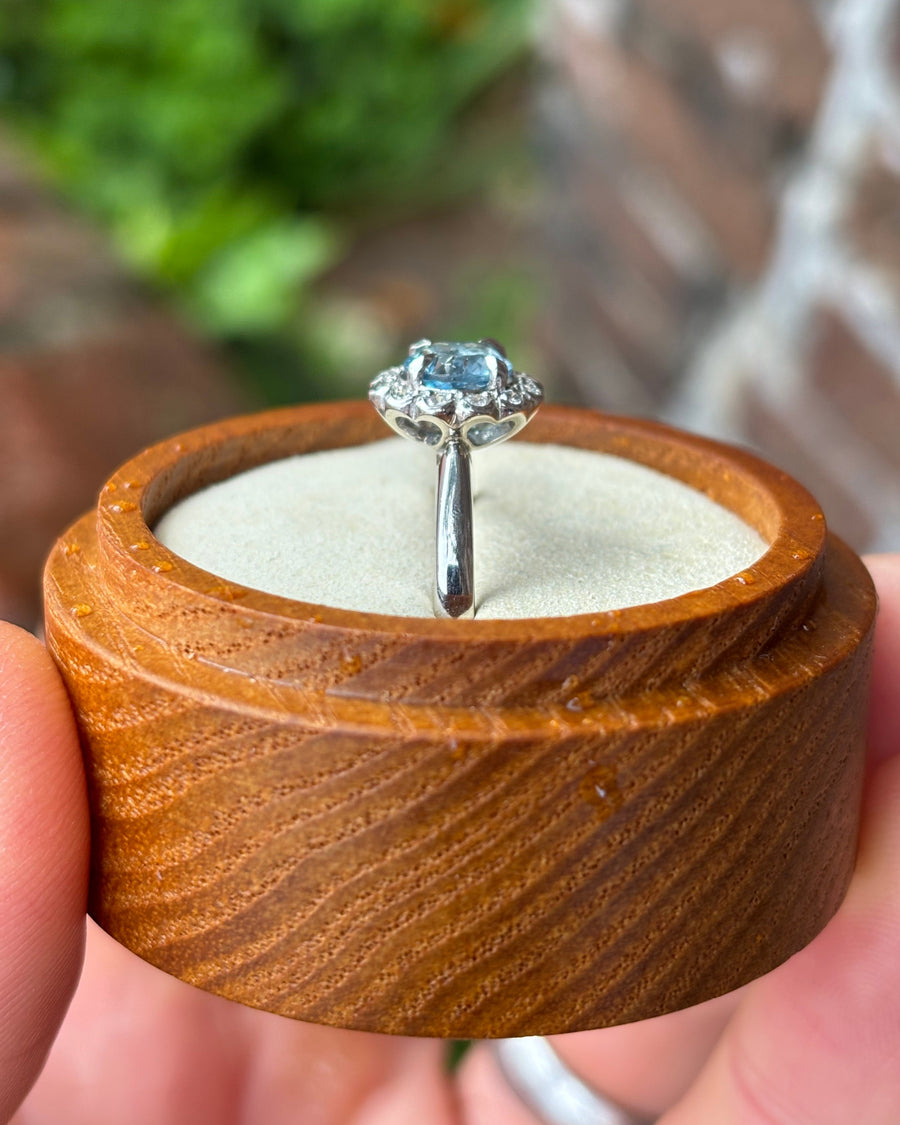 Aquamarine ring with a scalloped diamond cluster setting in white gold, displayed in a wooden ring box.