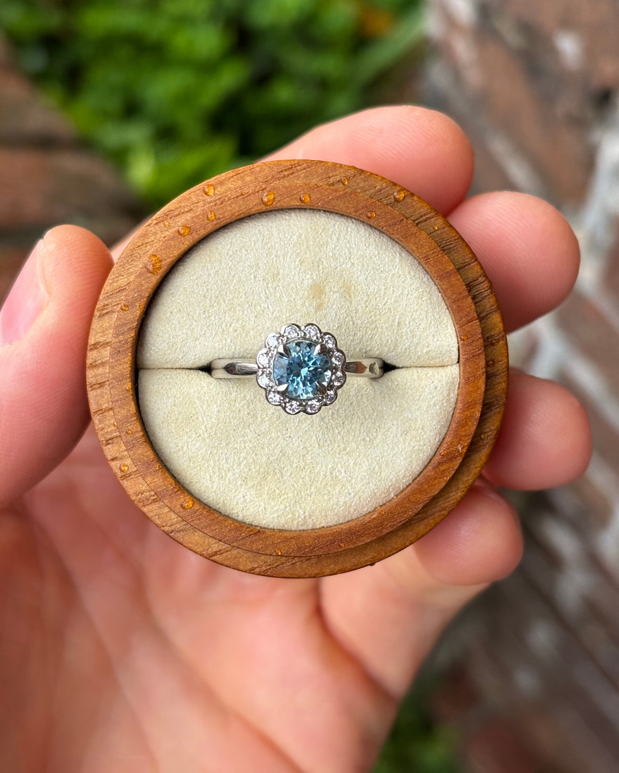 Platinum ring featuring a round aquamarine center stone surrounded by a scalloped diamond cluster halo.