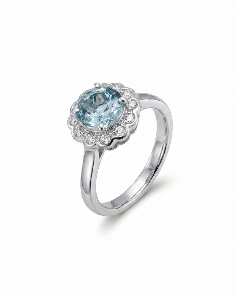 Silver ring with a round aquamarine surrounded by scalloped diamonds.