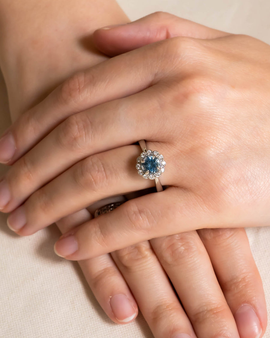 Silver ring with a round aquamarine surrounded by scalloped diamonds on a hand.