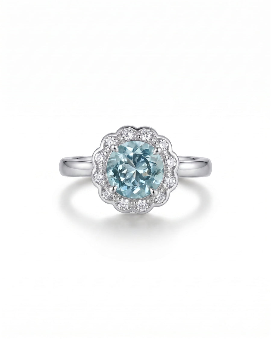 Silver ring with an oval aquamarine surrounded by scalloped diamonds.