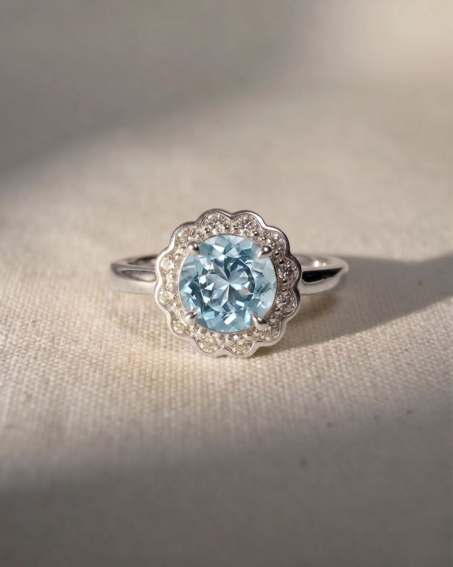 Platinum ring with a round aquamarine center stone and scalloped diamond halo.