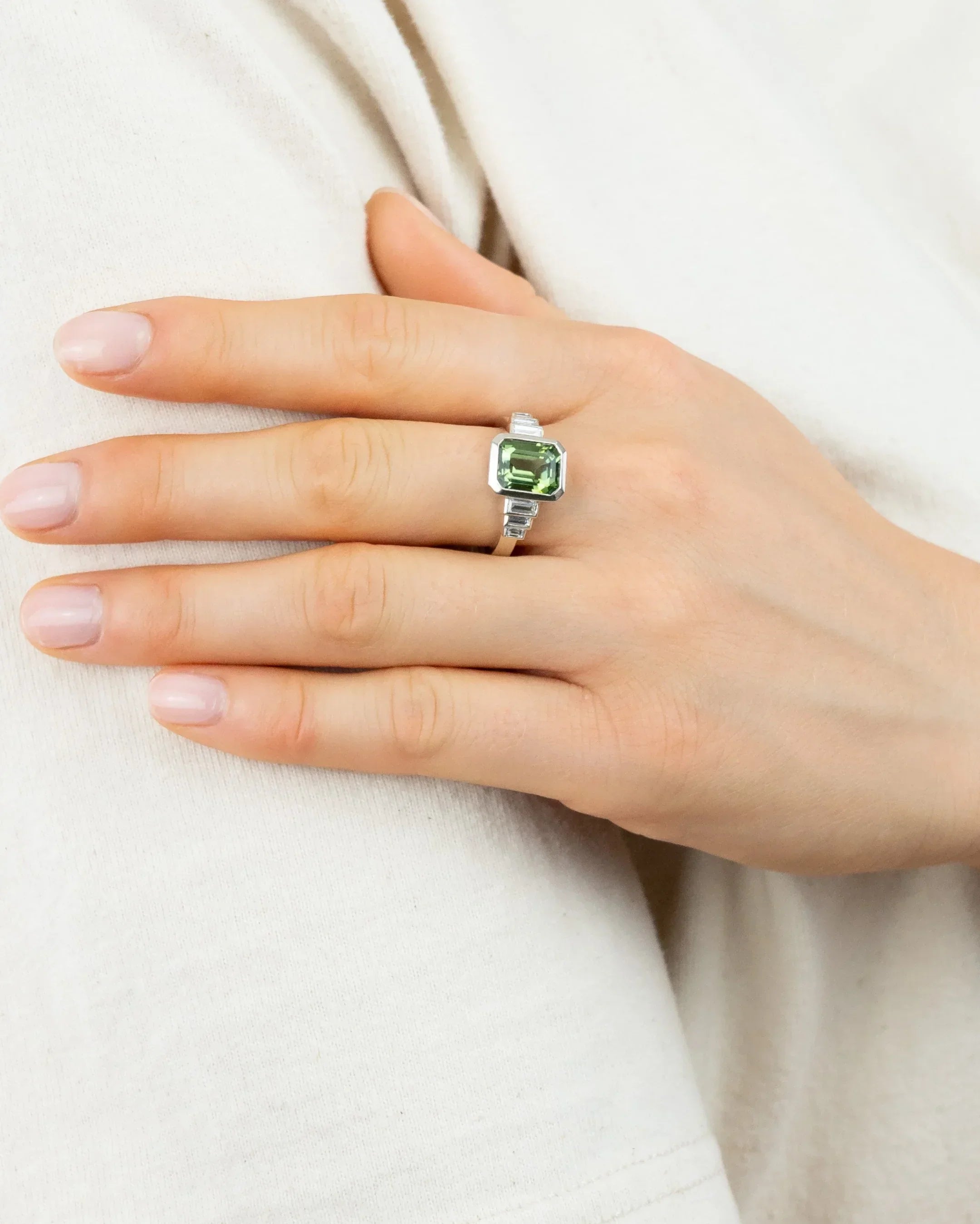 Hand wearing a silver ring with a green gemstone, showcasing elegant jewellery design