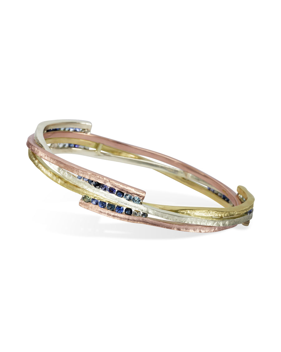 Mixed metal bangle with asymmetric bands of gold, rose gold, and silver, set with blue sapphires.
