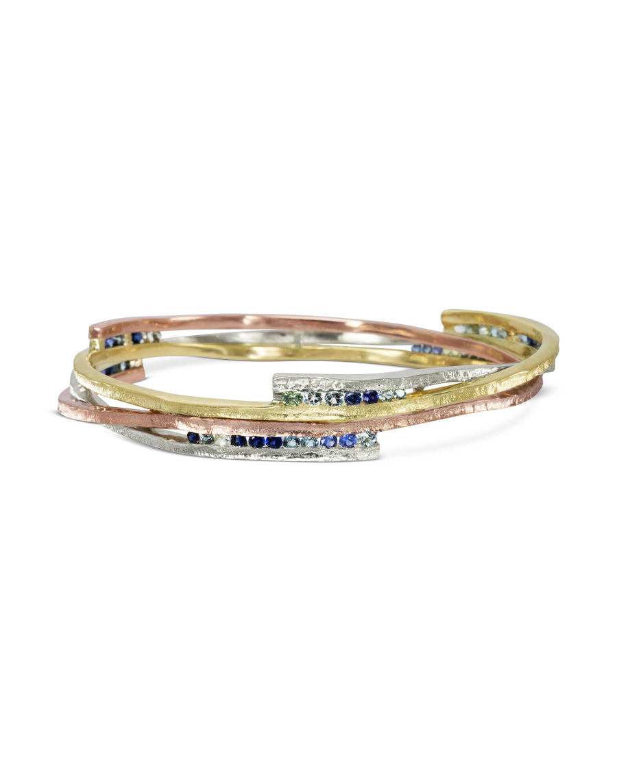 Asymmetric mixed metal bangle with blue sapphires.
