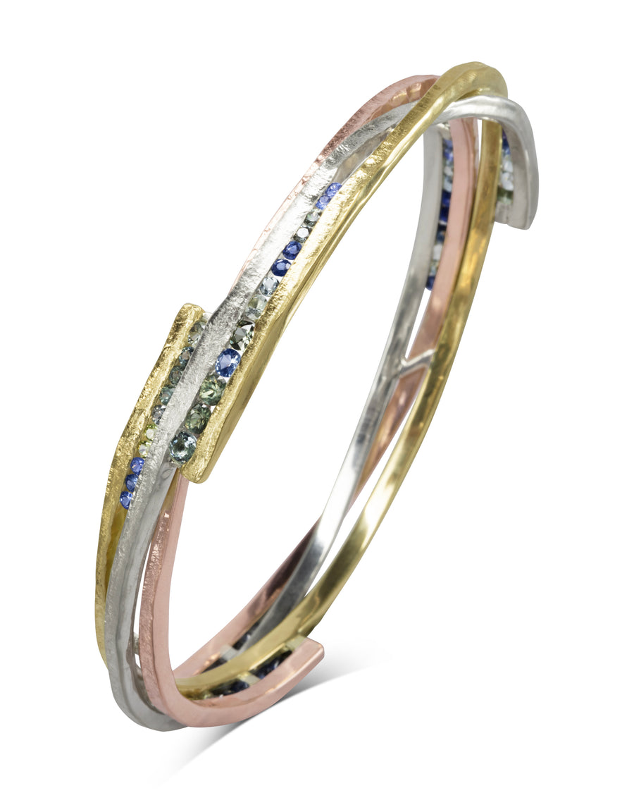 Asymmetric mixed metal bangle with blue and green sapphires.