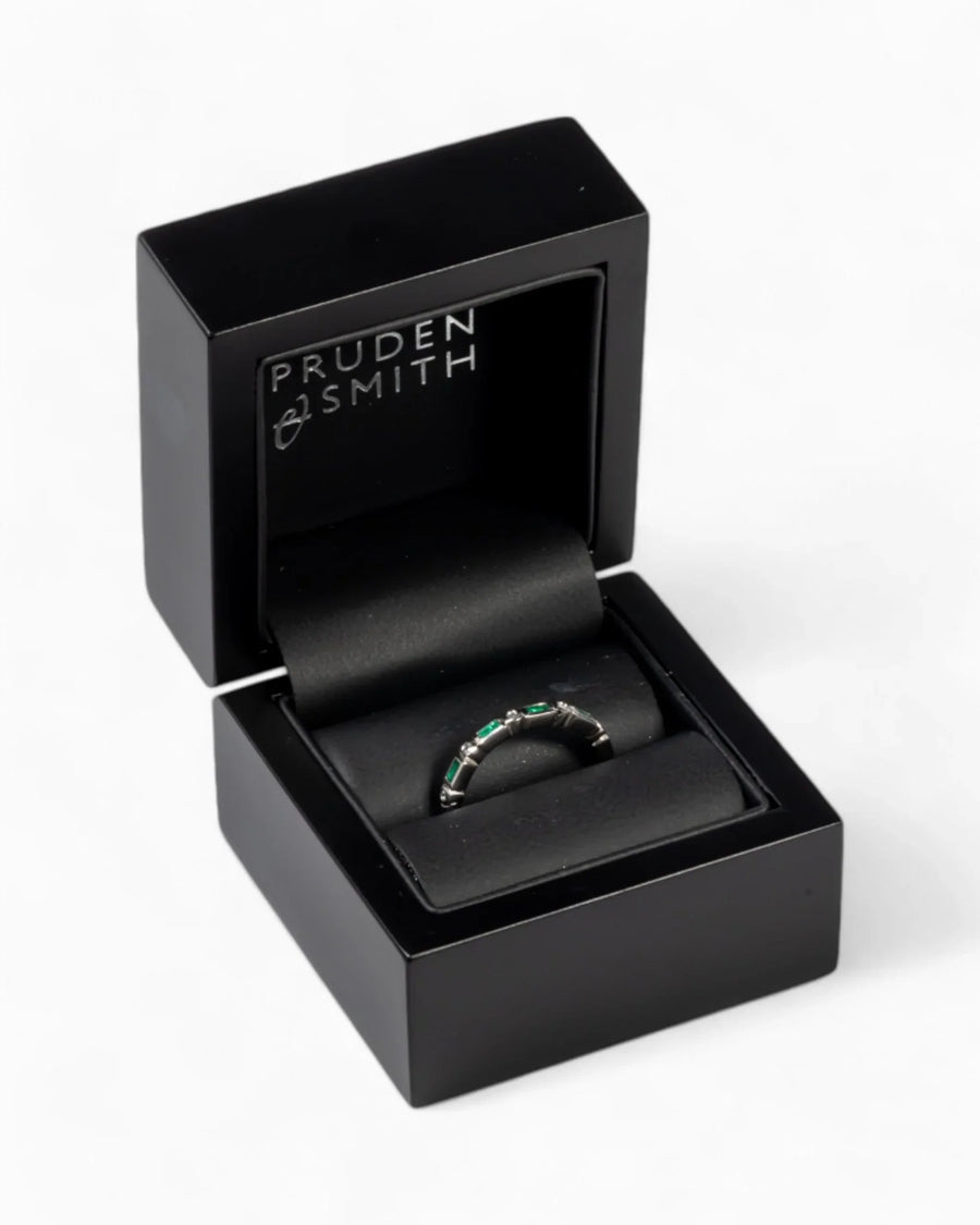 Silver eternity ring with baguette cut green gemstones in a black box.