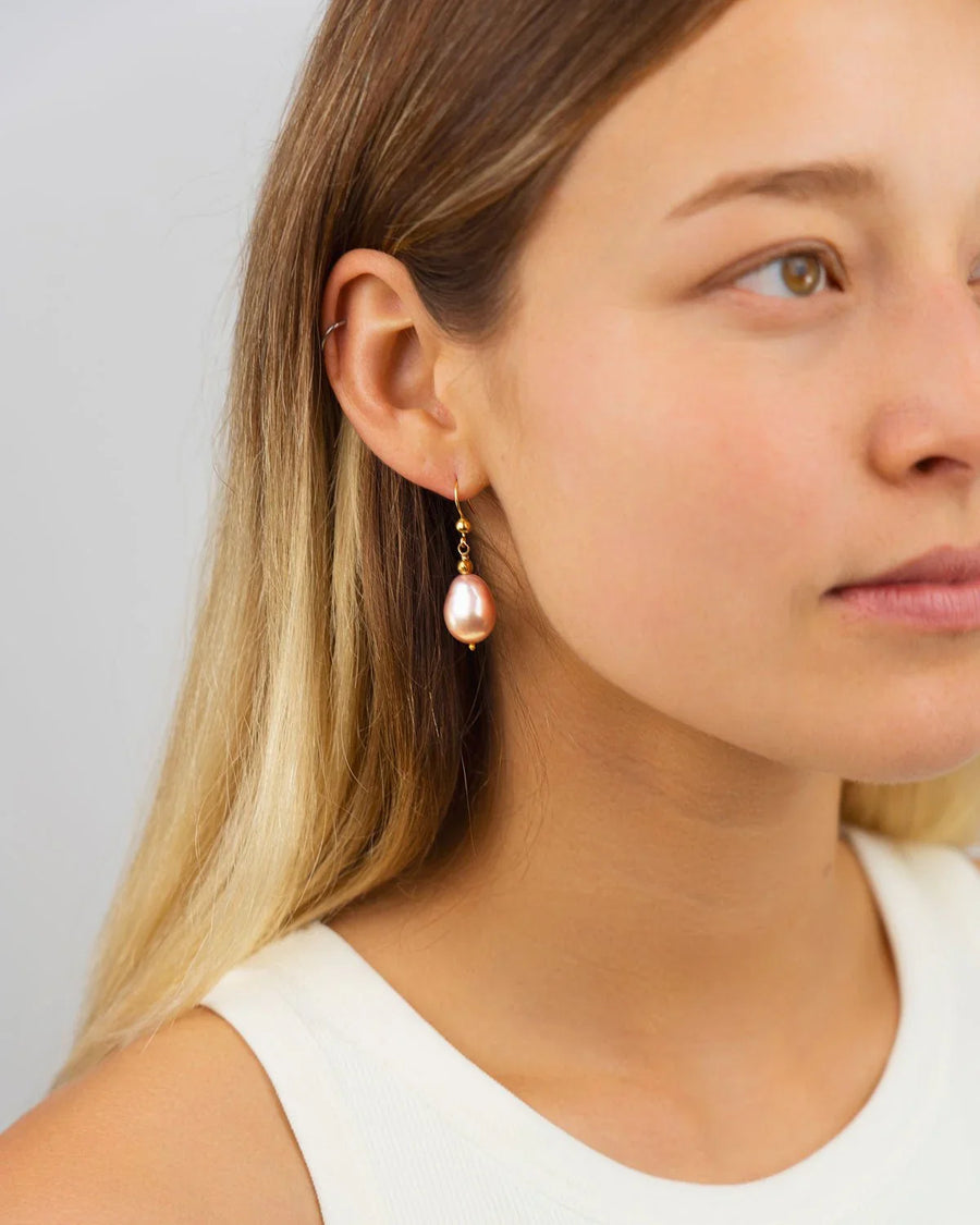 Pink baroque pearl drop earrings on gold hooks worn by a woman.