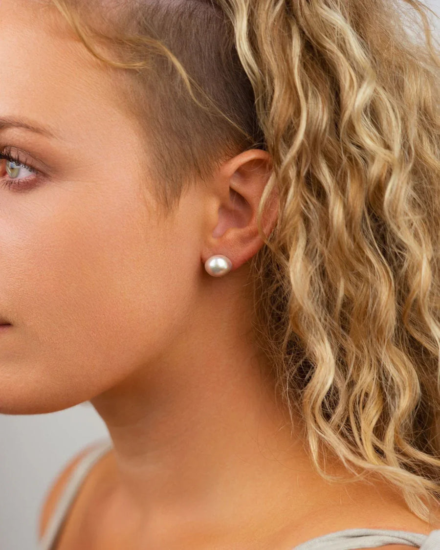White baroque pearl stud earring on a woman's ear.