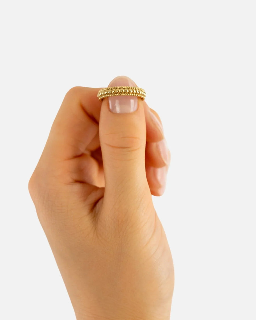 Hand holding a beaded three-row yellow gold ring against a white background