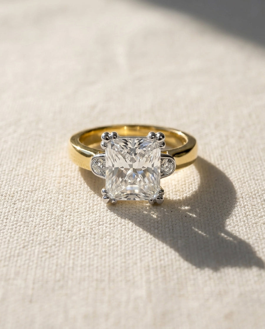 Yellow gold engagement ring with a large radiant cut diamond and two small side diamonds.