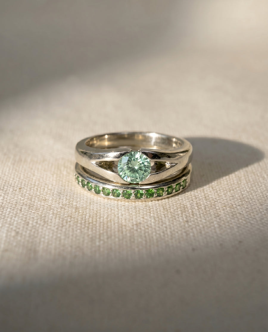 Platinum engagement ring with a round green diamond and a matching band with green gemstones.