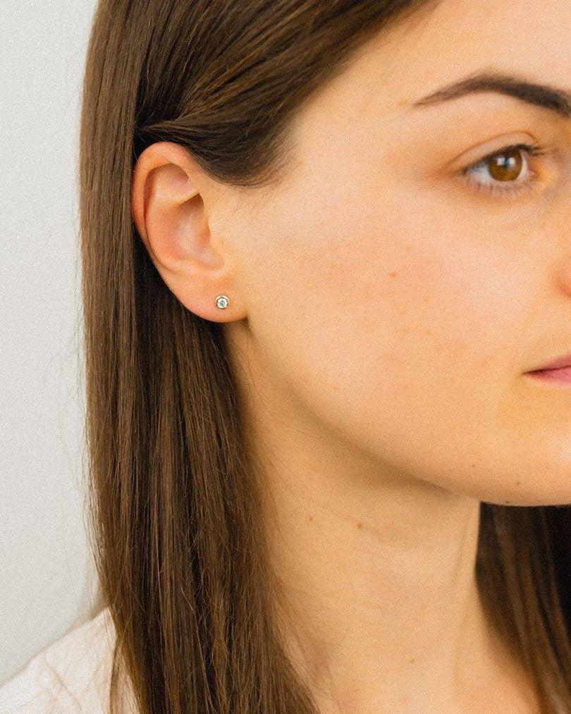 Silver bezel set diamond stud earrings on an ear.