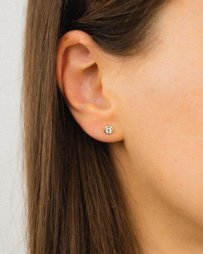 Gold bezel set diamond stud earring on an ear.