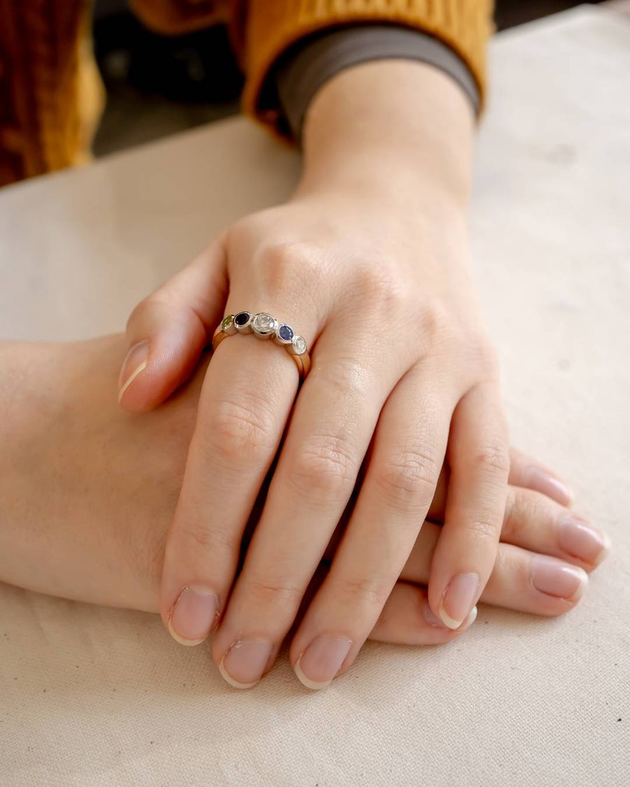 Gold eternity ring with five round birthstones: green, white, blue, and clear.