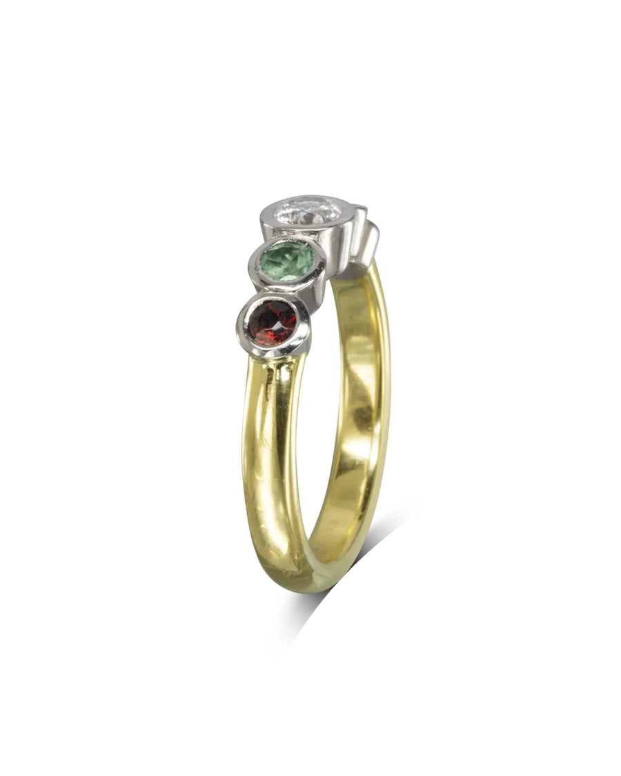 Gold and silver eternity ring with three bezel-set gemstones: clear, green, and red.