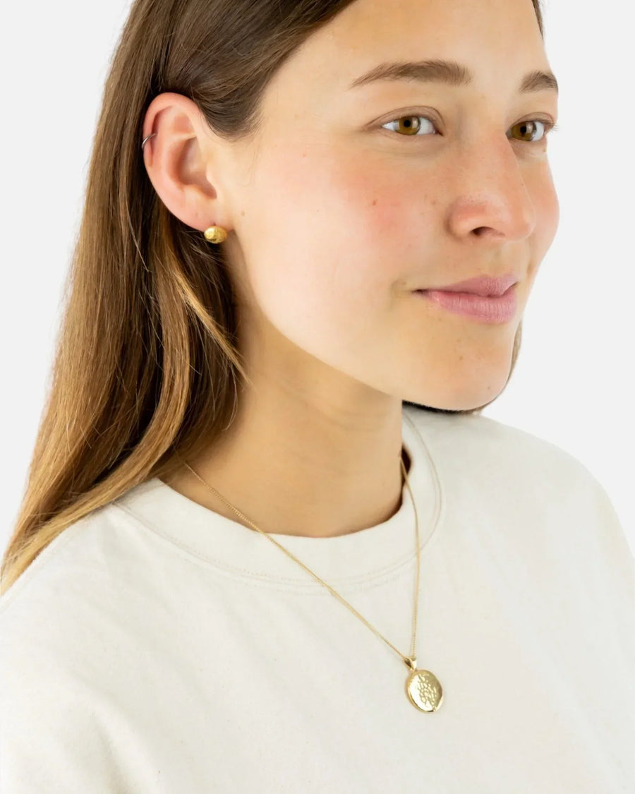 Woman wearing a hammered solid 9ct yellow gold coin pendant necklace and gold stud earring