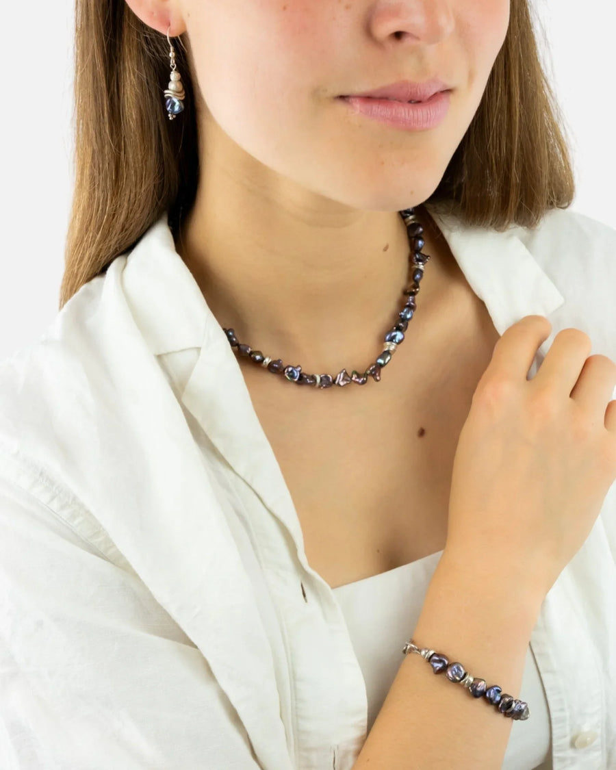 Woman wearing a black keshi pearl necklace, matching bracelet, and pearl drop earring