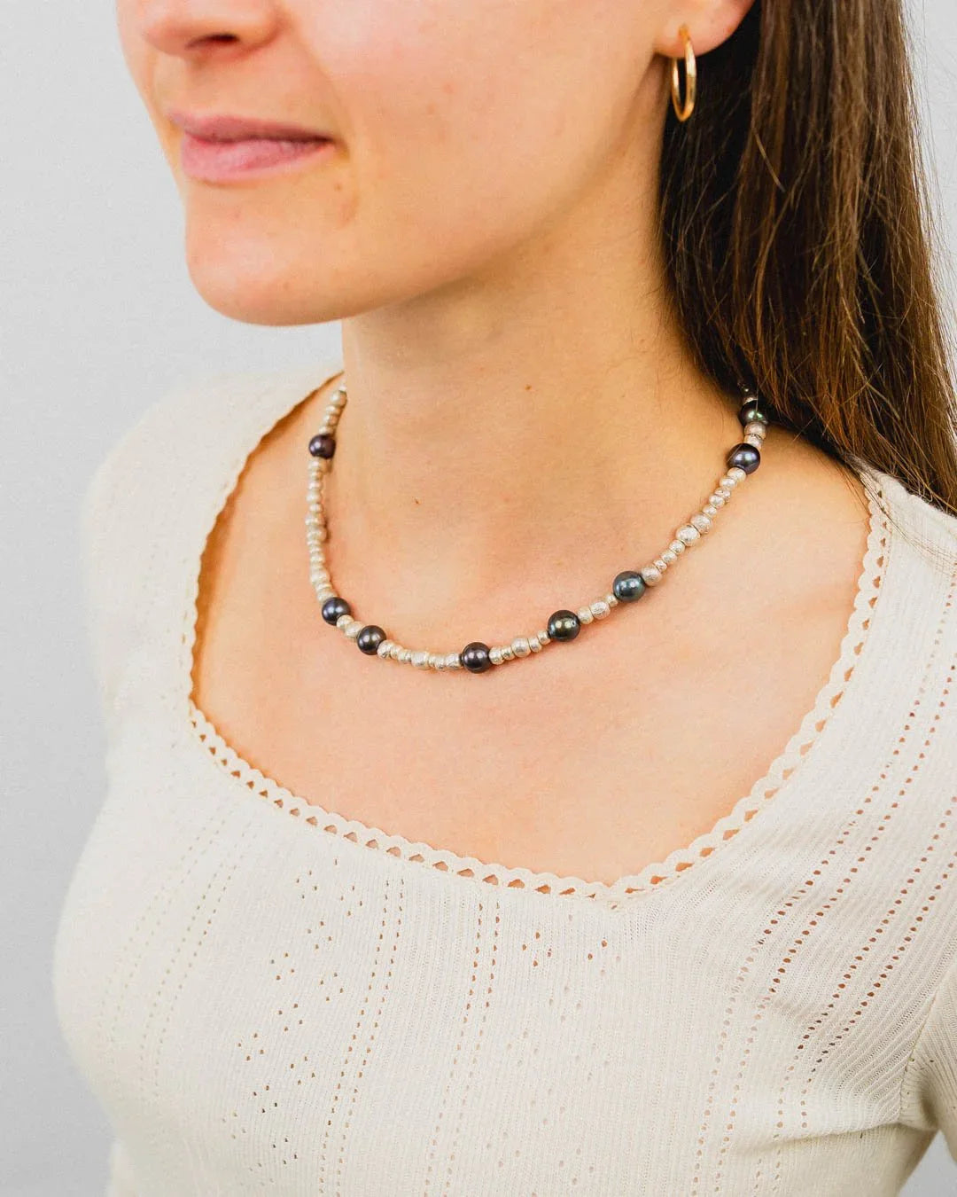 Woman wearing a black pearl and silver nugget necklace with a cream knit top