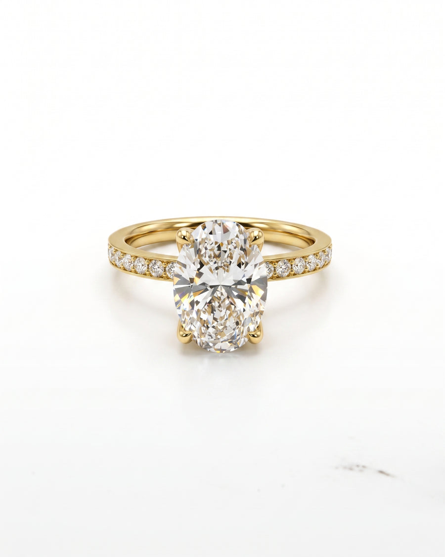 A yellow gold engagement ring featuring a large oval-cut center diamond and a pavé band with small round diamonds, set against a clean white background.