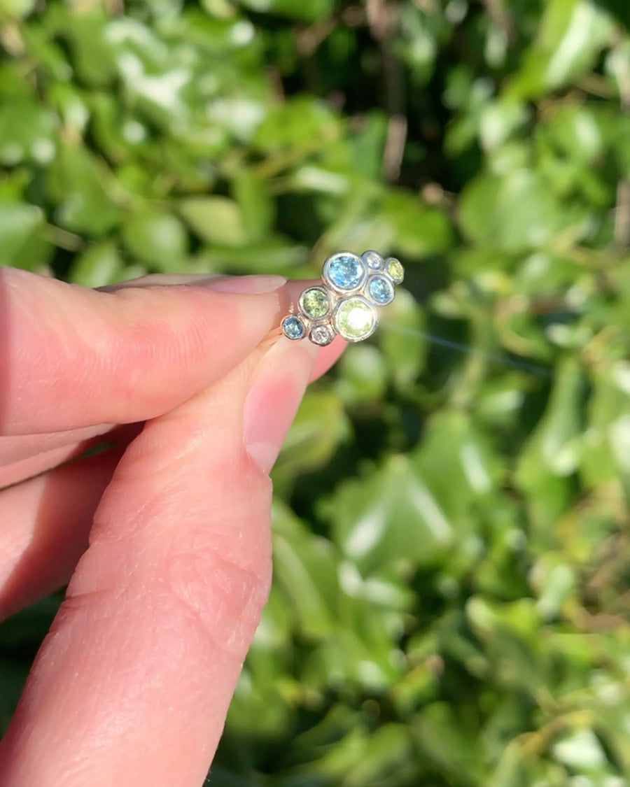 Hand holding a unique family gemstone ring with blue and green stones outdoors