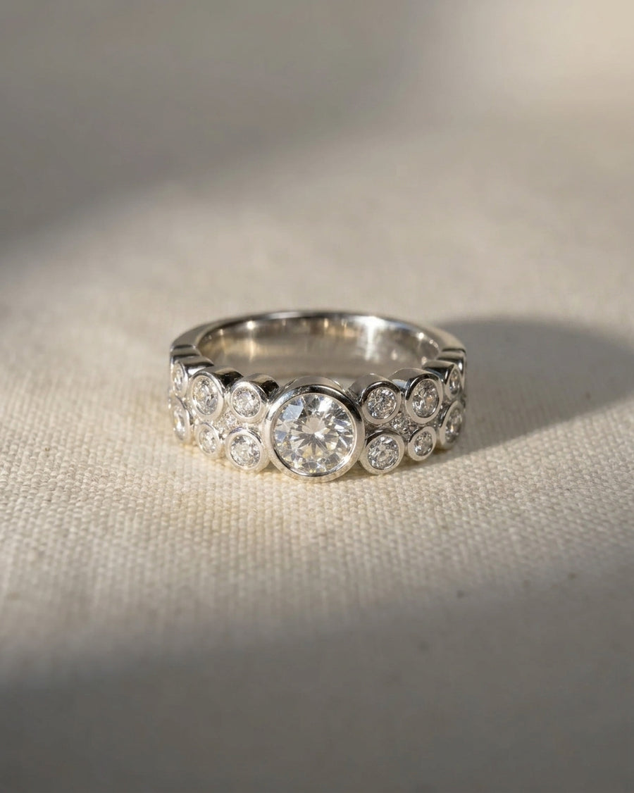 White gold eternity ring with a large central diamond surrounded by smaller bezel-set diamonds.