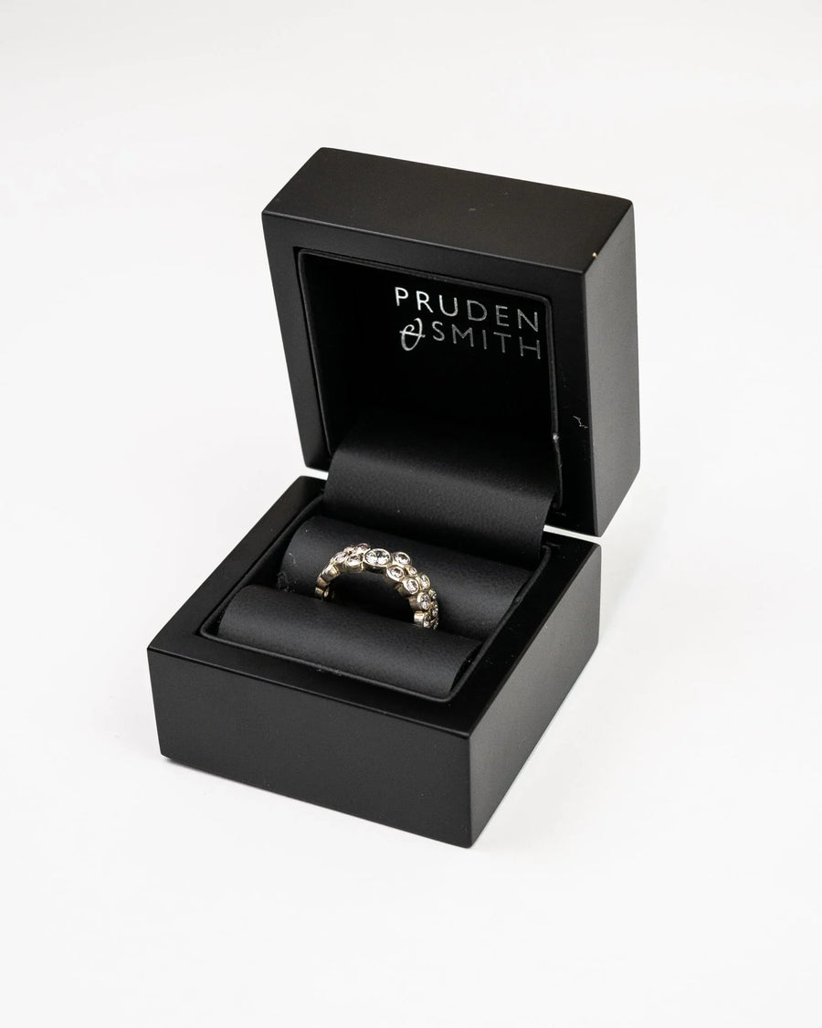 Gold eternity ring with round diamonds in a black ring box.