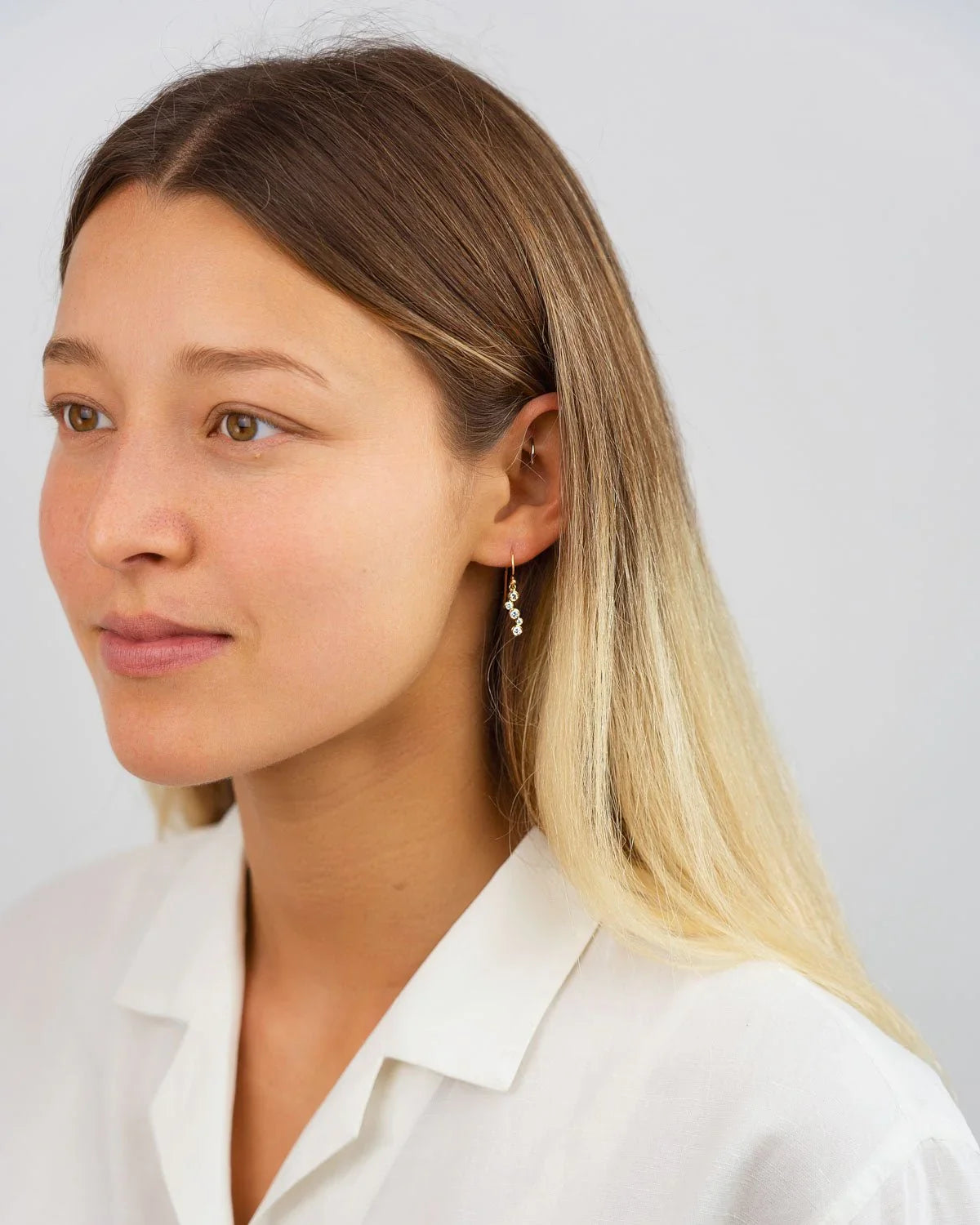 Woman wearing drop earrings with diamonds on yellow gold, minimal and elegant style