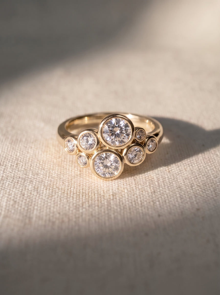 Gold ring featuring a cluster of round diamonds in bezel settings on a textured fabric background.